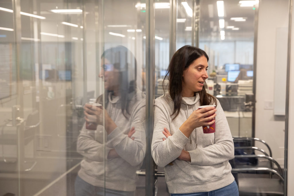 030122_Viking-CT_Candid-Office_0768_Lo-Res Woman leaning against a glass wall while holding her coffee.