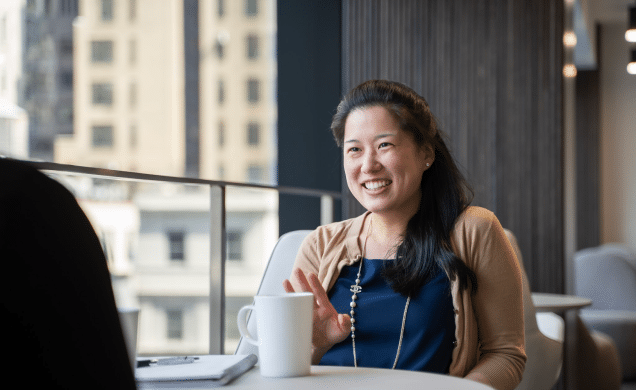 Colleagues sit next to each other at a conference table and smile to someone off camera.