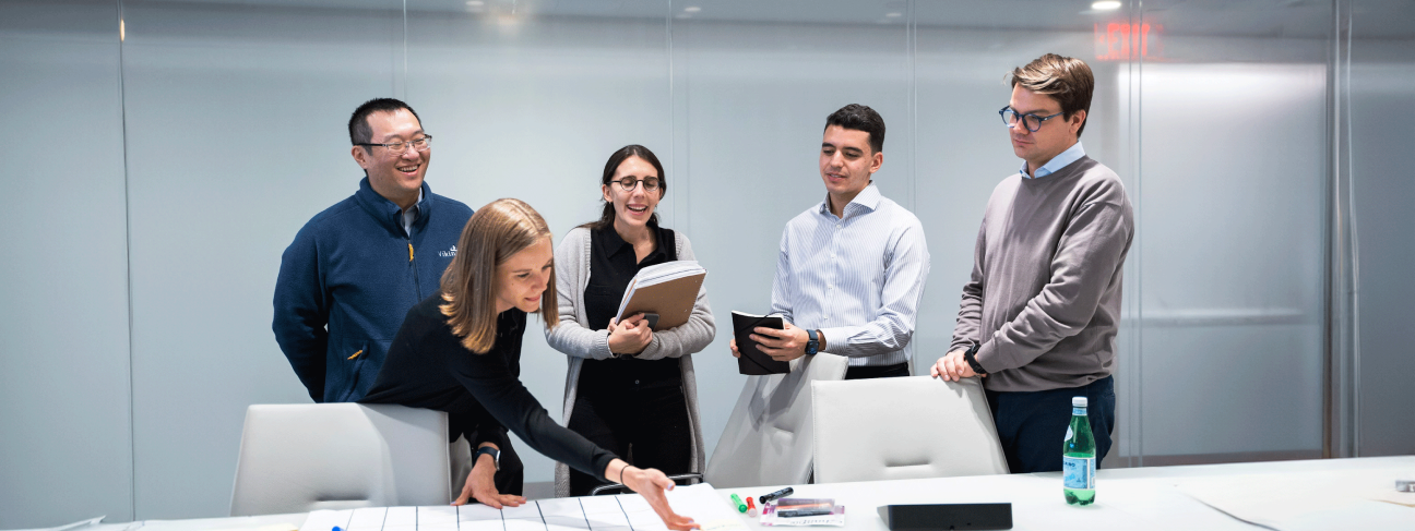 Five colleagues sit around a long table in a conference room with glass walls.